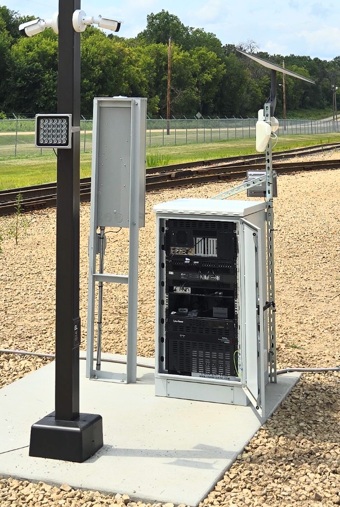 Open equipment rack with networking gear, solar panel, and cameras at a rail yard tracking installation