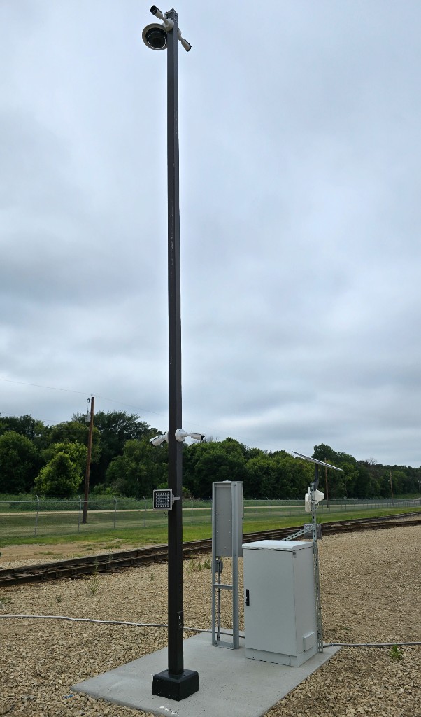 Completed camera pole installation with utility cabinets at a rail yard tracking site